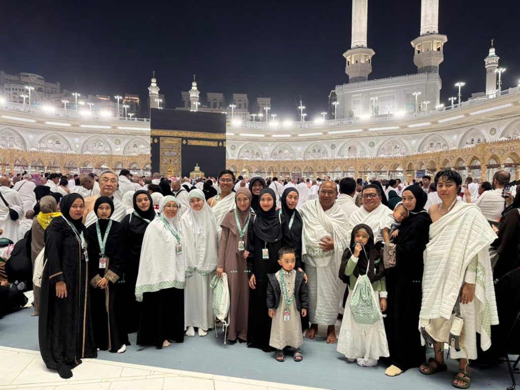 Rombongan jemaah dan keluarga Safari Suci tersenyum nyaman saat berfoto di depan Ka'bah, menikmati ibadah premium tanpa perlu repot mengurus umrah mandiri.